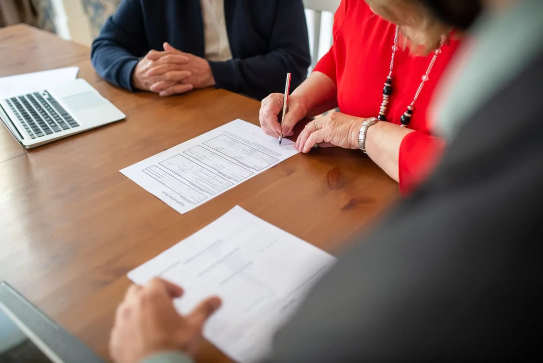 Home buyers signing closing documents at a wooden table with a laptop. Photo by Kampus Production on Pexels