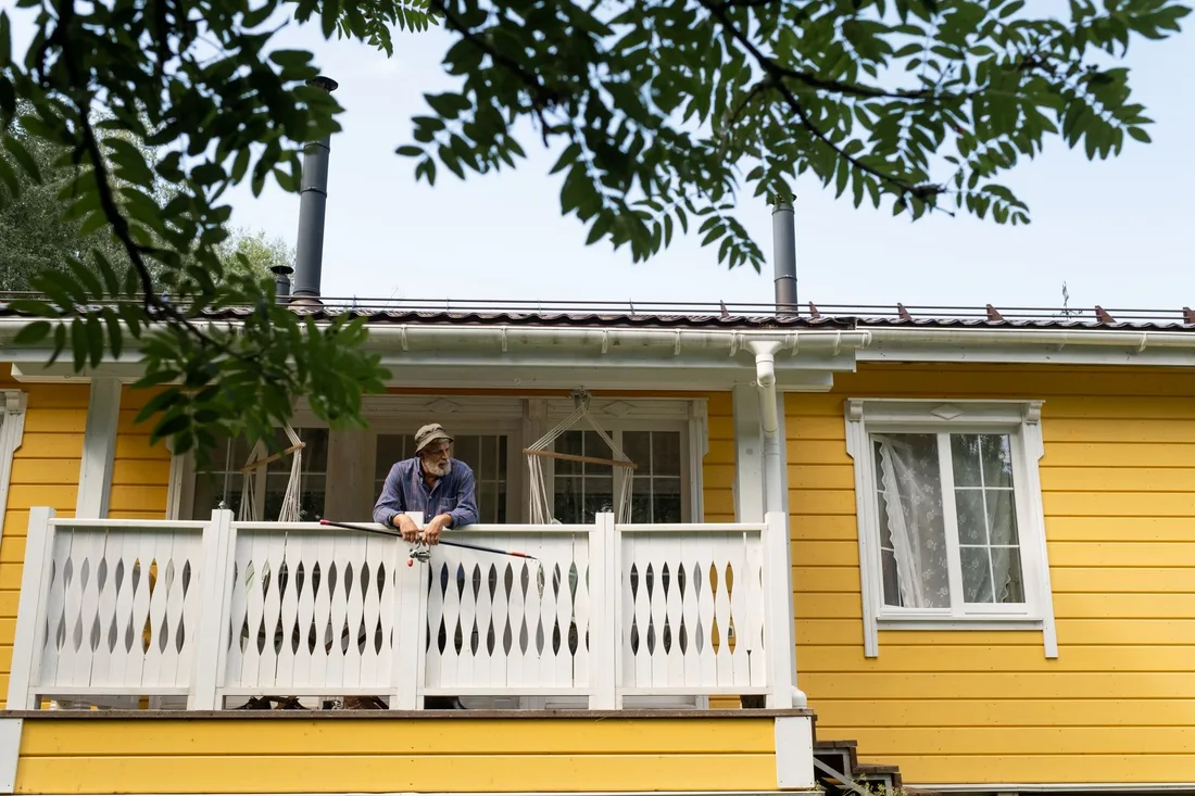 Homeowner standing on the porch of a yellow house under trees. Photo by Ron Lach on Pexels