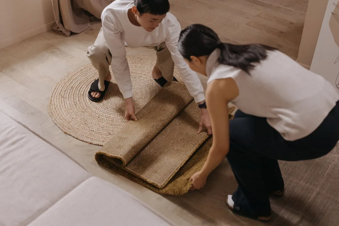 Two people lifting and rolling up a soaked carpet in a living room. Photo by cottonbro studio on Pexels