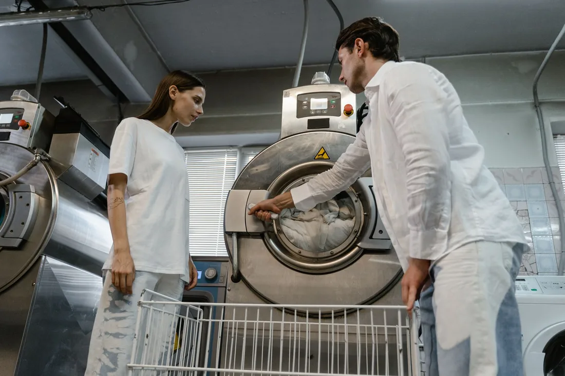 Man and woman operating industrial washing machines in a laundry facility. Photo by Tima Miroshnichenko on Pexels