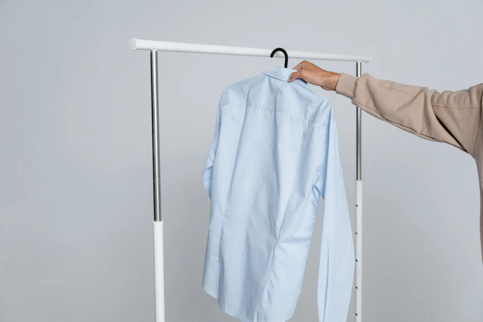 Hand holding out a freshly cleaned light blue shirt on a hanger and rail. Photo by MART  PRODUCTION on Pexels