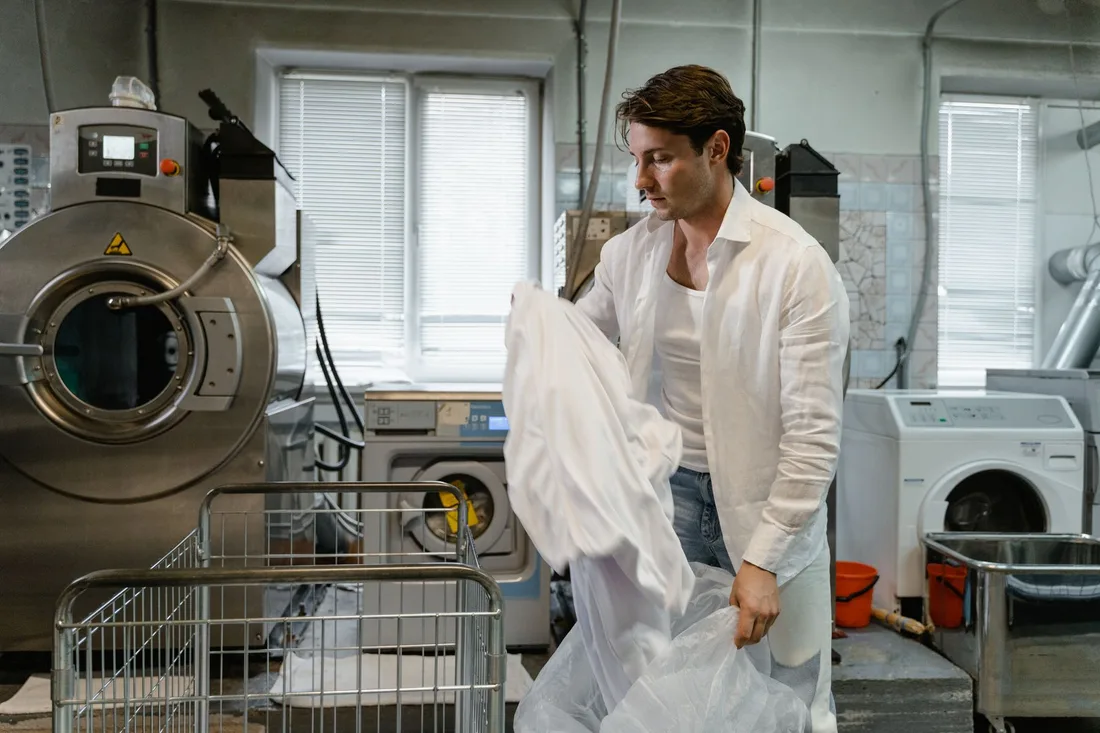 Man organizing laundry in a modern industrial facility with large washing machines. Photo by Tima Miroshnichenko on Pexels