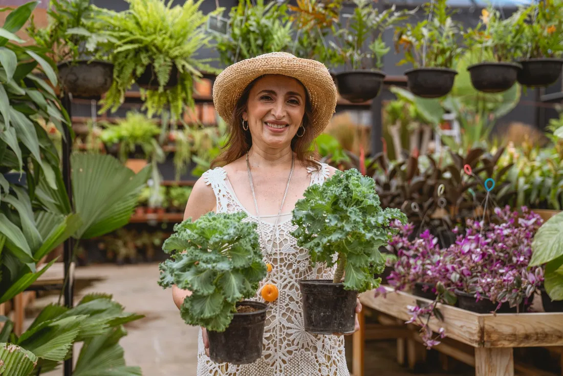 Smiling woman in a straw hat holding two potted plants in a garden center. Photo by Los Muertos Crew on Pexels