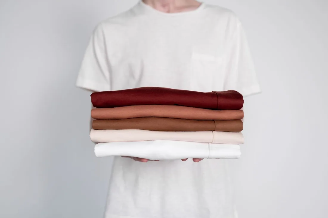 Person holding a neat stack of folded clean t-shirts. Photo by Ron Lach on Pexels