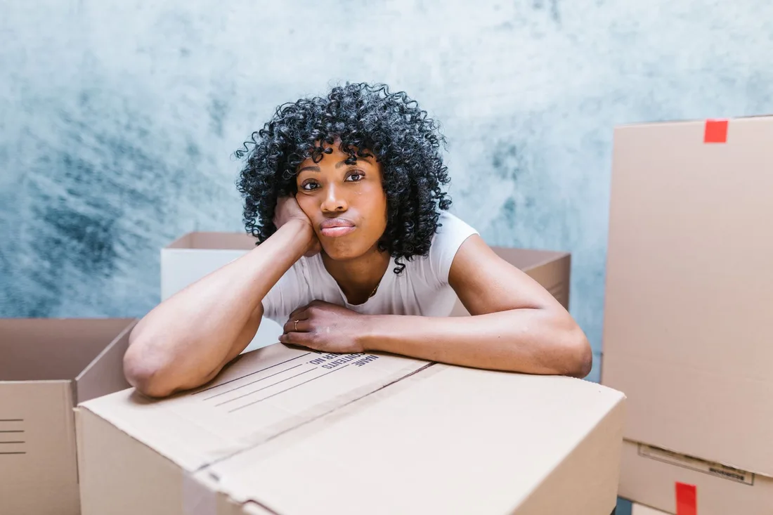 Tired woman leaning on a moving box while packing and relocating to a new home. Photo by RDNE Stock project on Pexels