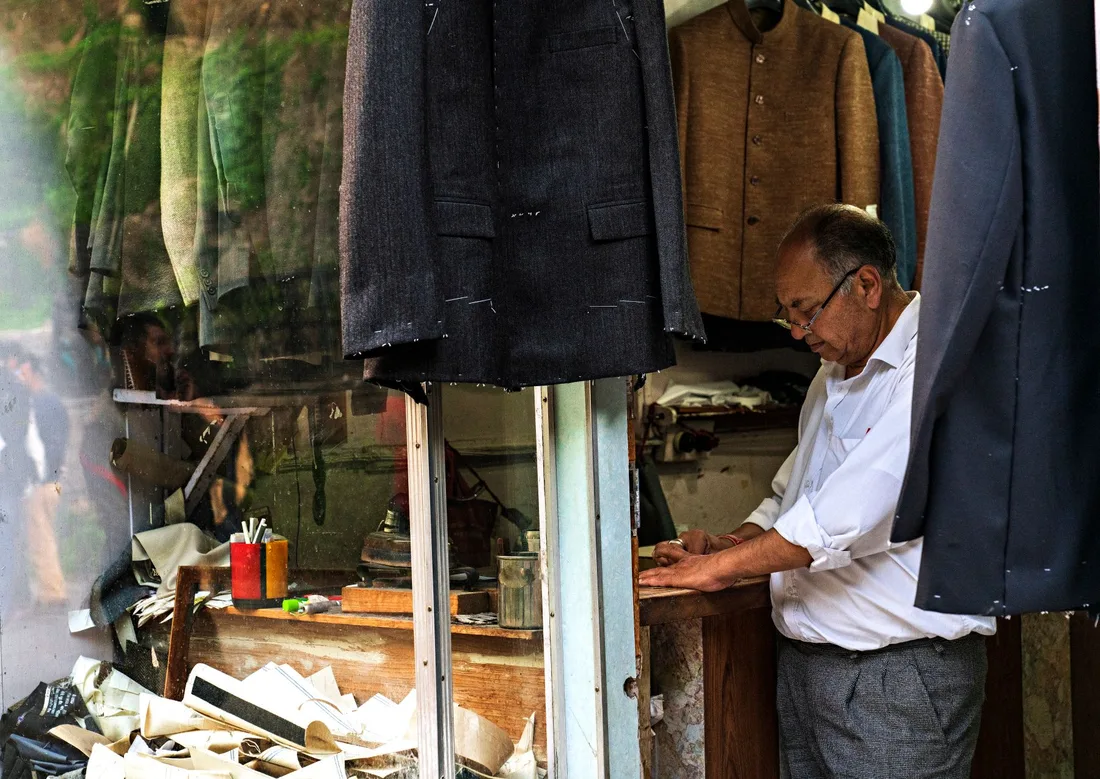 An experienced tailor working in a classic sewing shop surrounded by suits and materials. Photo by Nishant Aneja on Pexels