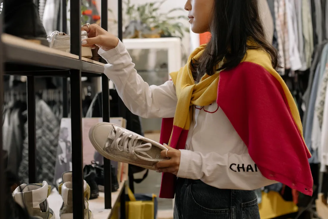 A woman browsing sneakers in a thrift store, showcasing the retail shopping experience. Photo by cottonbro studio on Pexels