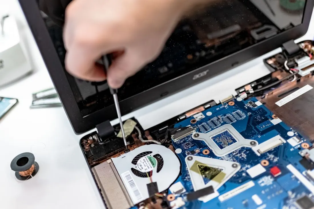 A technician unscrewing the hinge of an open laptop to reach the cooling fan and motherboard. Photo by IT services EU on Pexels