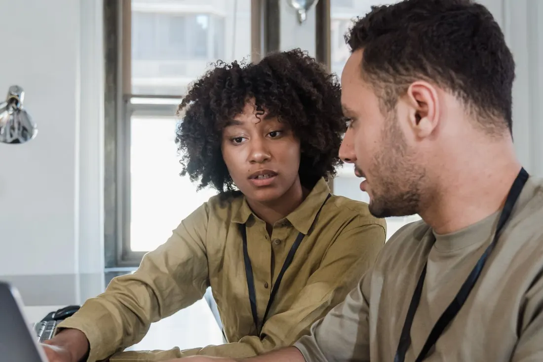 Two colleagues at a laptop in a small office, one pointing at the screen. Photo by Mizuno K on Pexels