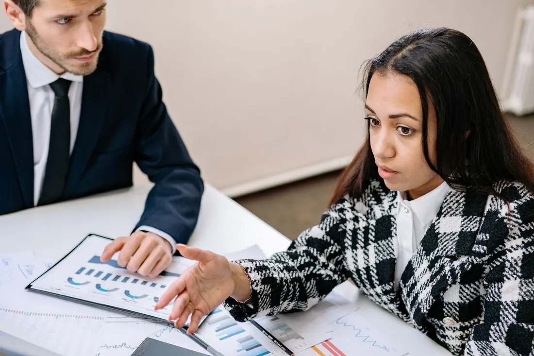 Two people at a white table reviewing printed bar charts. Photo by Yan Krukau on Pexels