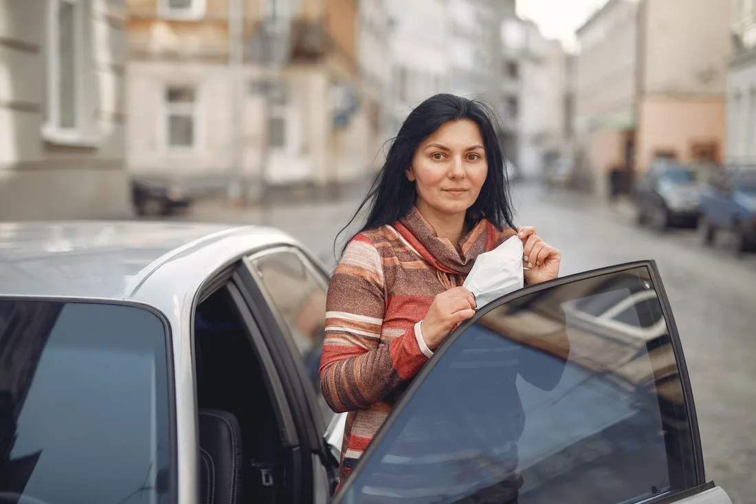 Woman standing beside an open car door on a city street holding paperwork. Photo by Gustavo Fring on Pexels