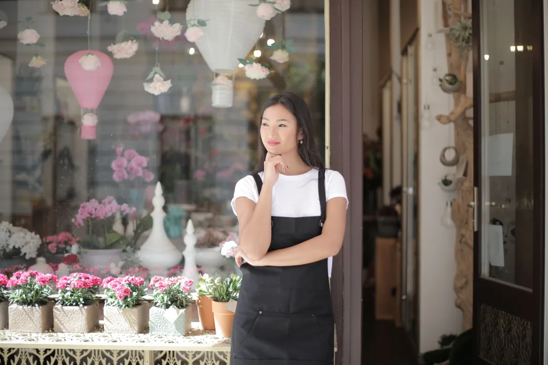 Woman shop owner standing at the doorway of her flower shop. Photo by Andrea Piacquadio on Pexels