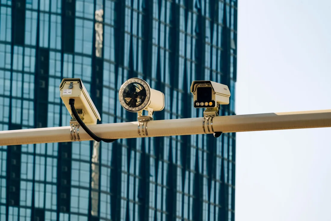 Security cameras mounted on a pole against a glass office tower. Photo by Star Zhang on Pexels