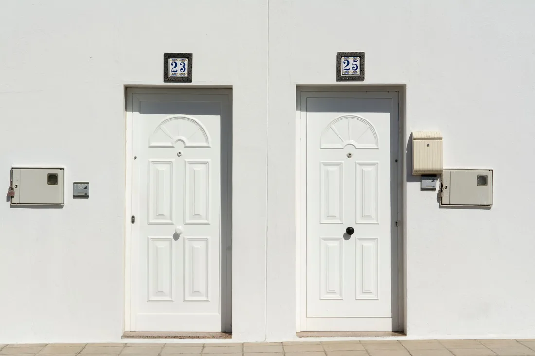 Two white apartment entry doors each with an intercom unit on the wall. Photo by Jan van der Wolf on Pexels
