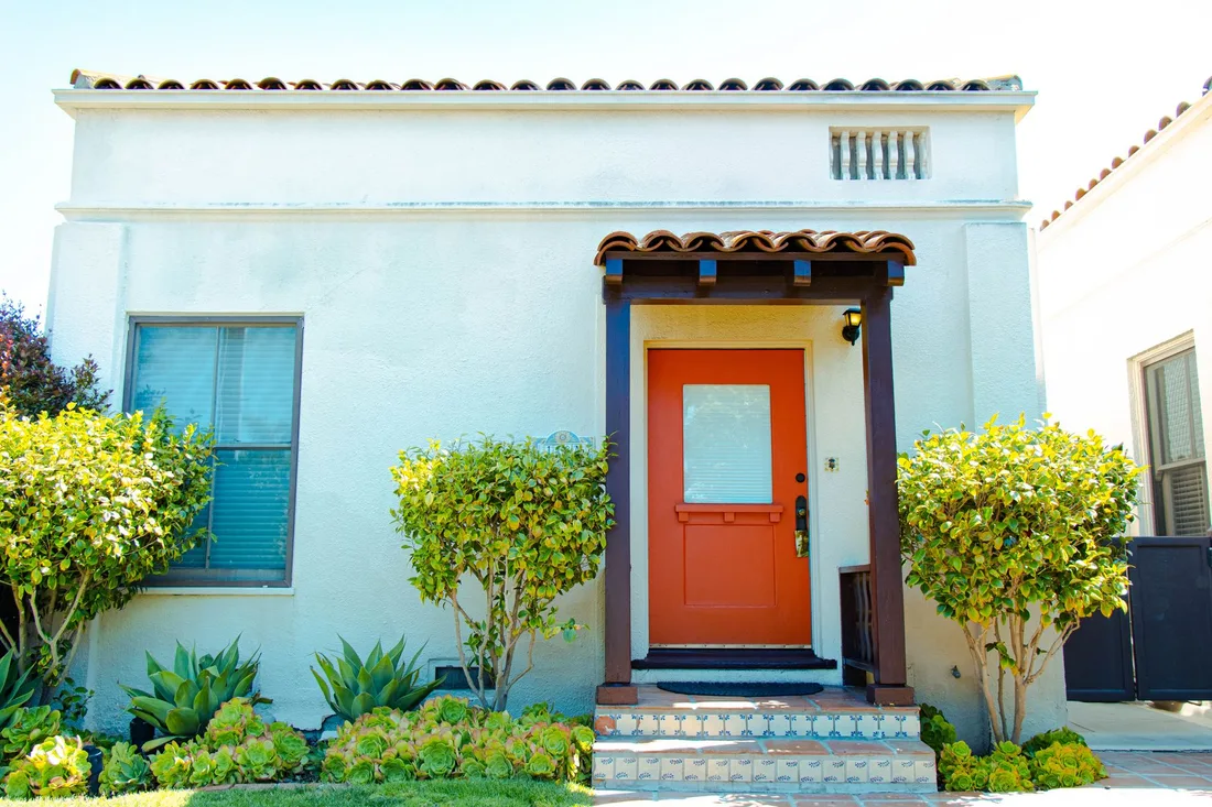 White house with a bright orange front door and trimmed shrubs. Photo by Phil Evenden on Pexels
