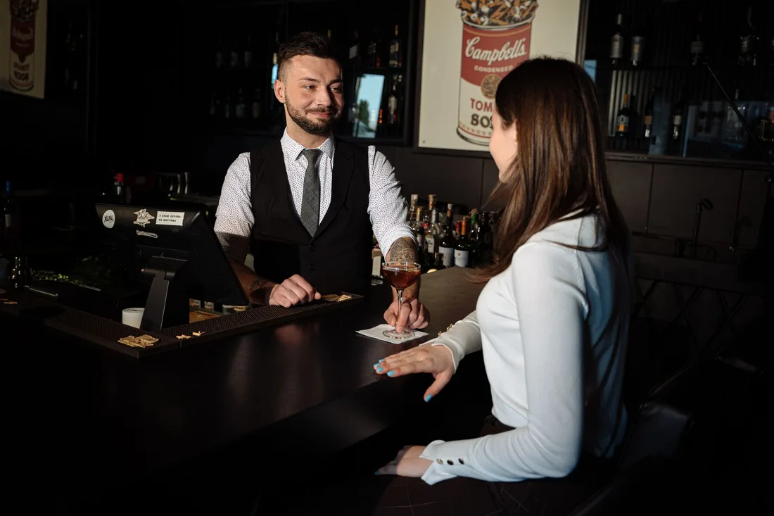 Bartender serving a cocktail to a customer at a dimly lit bar, creating a cozy atmosphere. Photo by AI25.Studio  Studio on Pexels