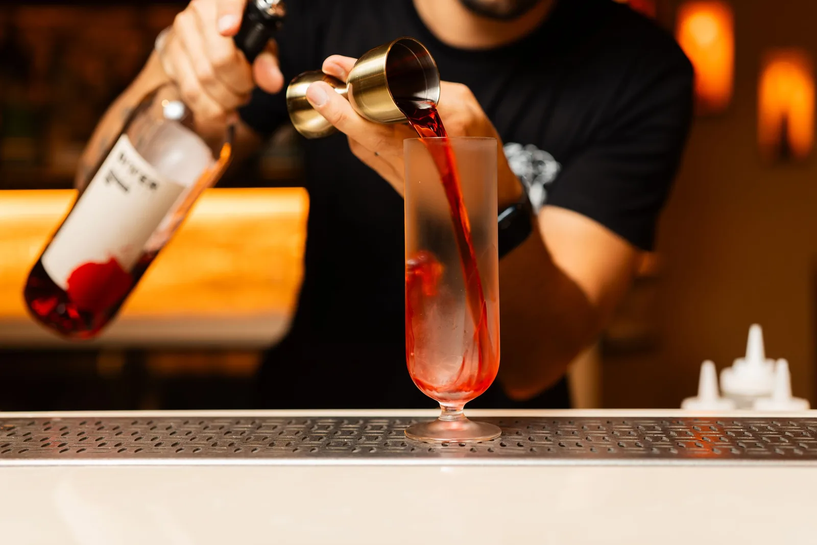 Close-up of a bartender pouring a vibrant red cocktail into a glass at a bar counter. Photo by Andrea Prochilo on Pexels