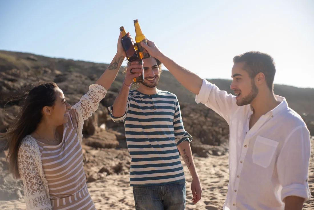 Friends raising bottles in a cheerful toast on a sunny beach. Photo by Kampus Production on Pexels