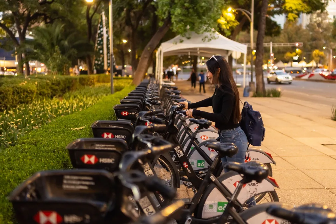 A woman selects a public rental bike from a bicycle stand in Mexico City during twilight. Photo by Julio Lopez on Pexels
