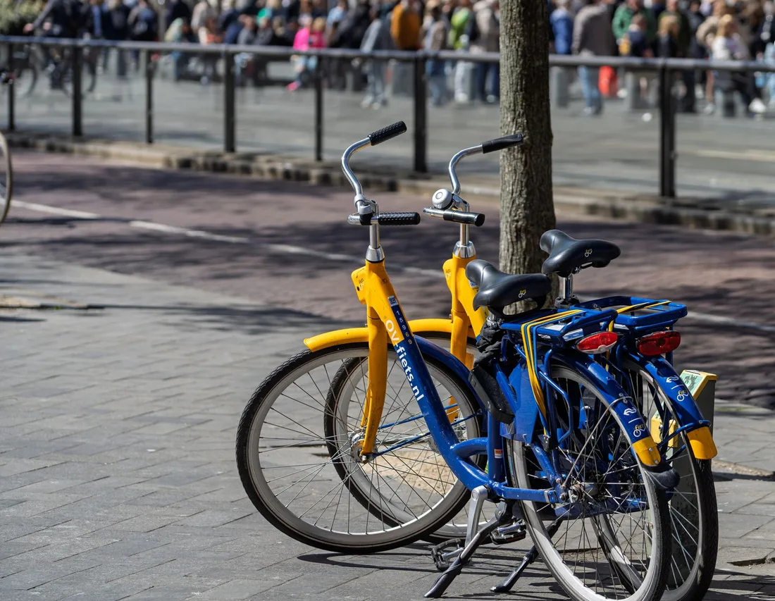 Blue and yellow rental bicycles parked on a vibrant urban street with pedestrians in the background. Photo by Martijn Stoof on Pexels