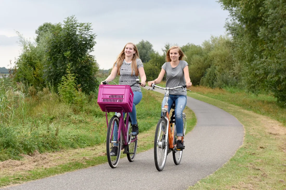 Two smiling women riding bicycles along a green path. Photo by Arthur Krijgsman on Pexels