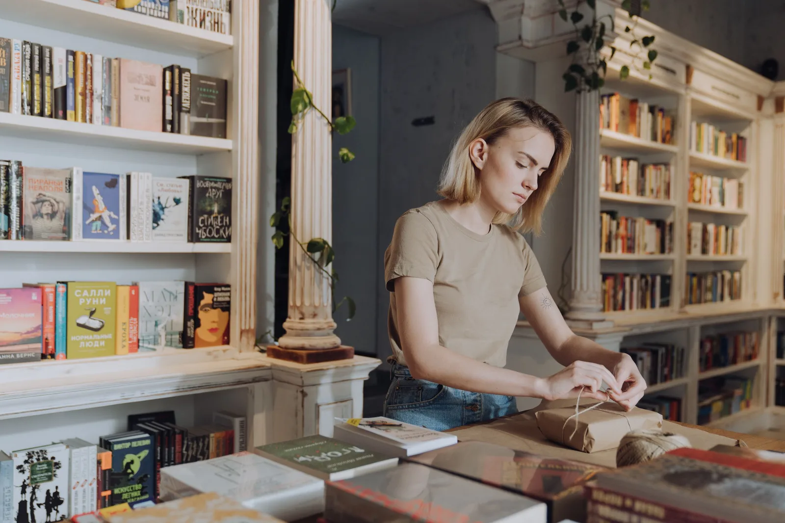 Young woman wrapping books in a warm, inviting bookshop with bookshelves full of literature around her. Photo by cottonbro studio on Pexels