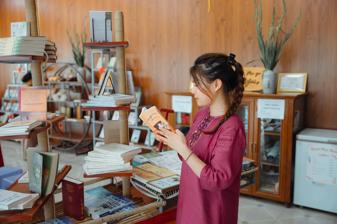Smiling woman browsing books in a warm, cozy bookstore. Photo by HONG SON on Pexels