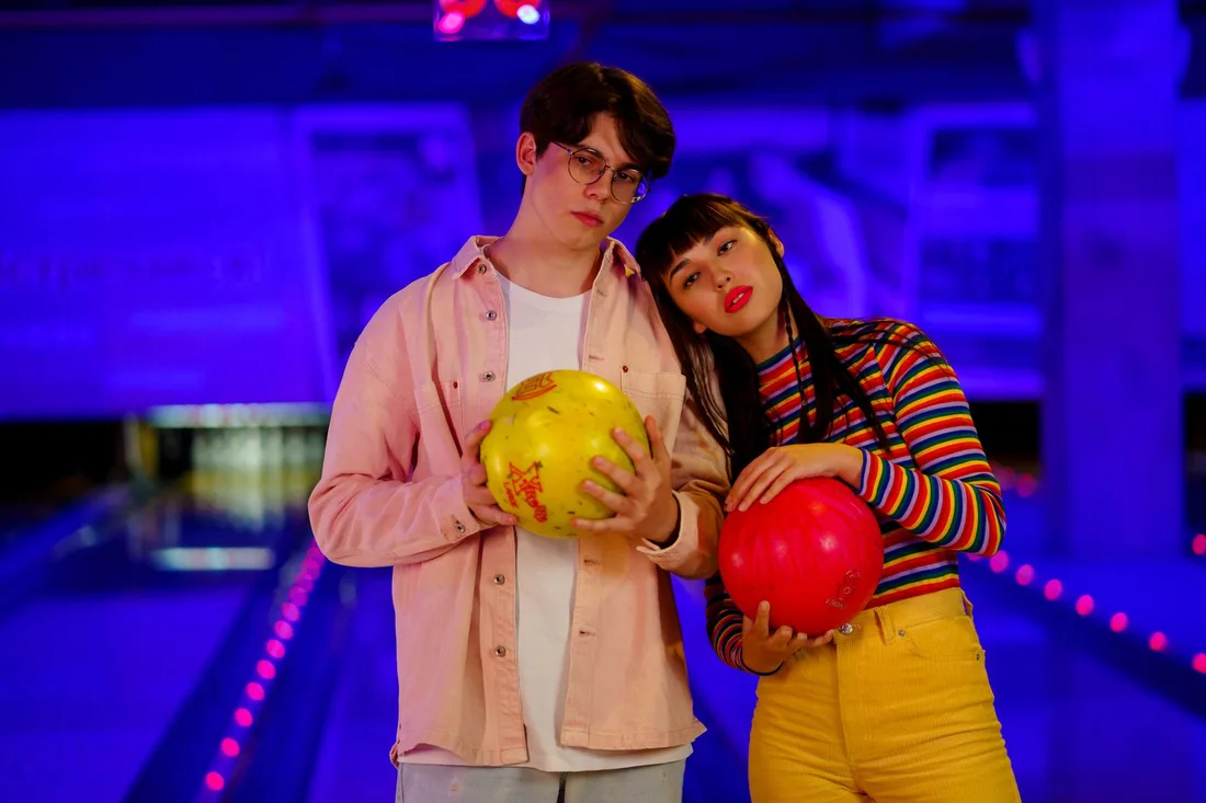 Young couple holding colorful bowling balls in a neon bowling alley. Photo by cottonbro studio on Pexels