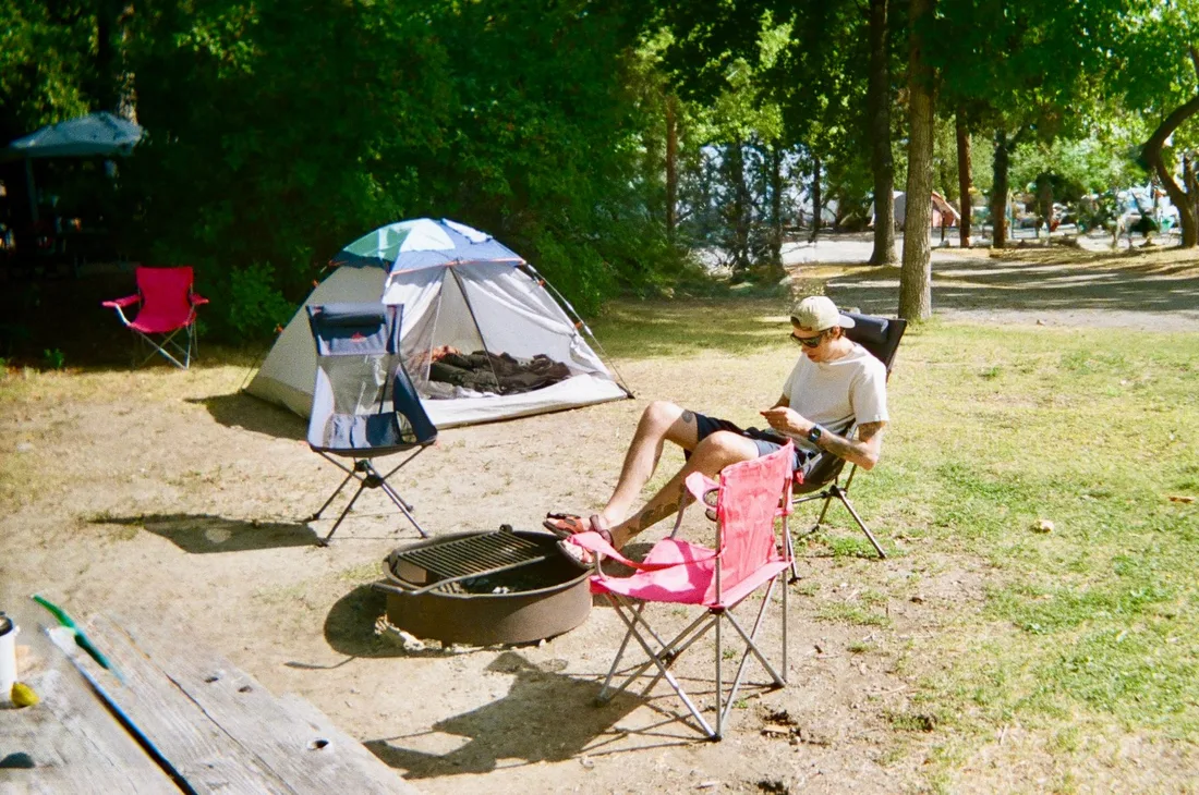 Man relaxing at a campsite with tent and chairs under trees. Photo by Rufina Rusakova on Pexels