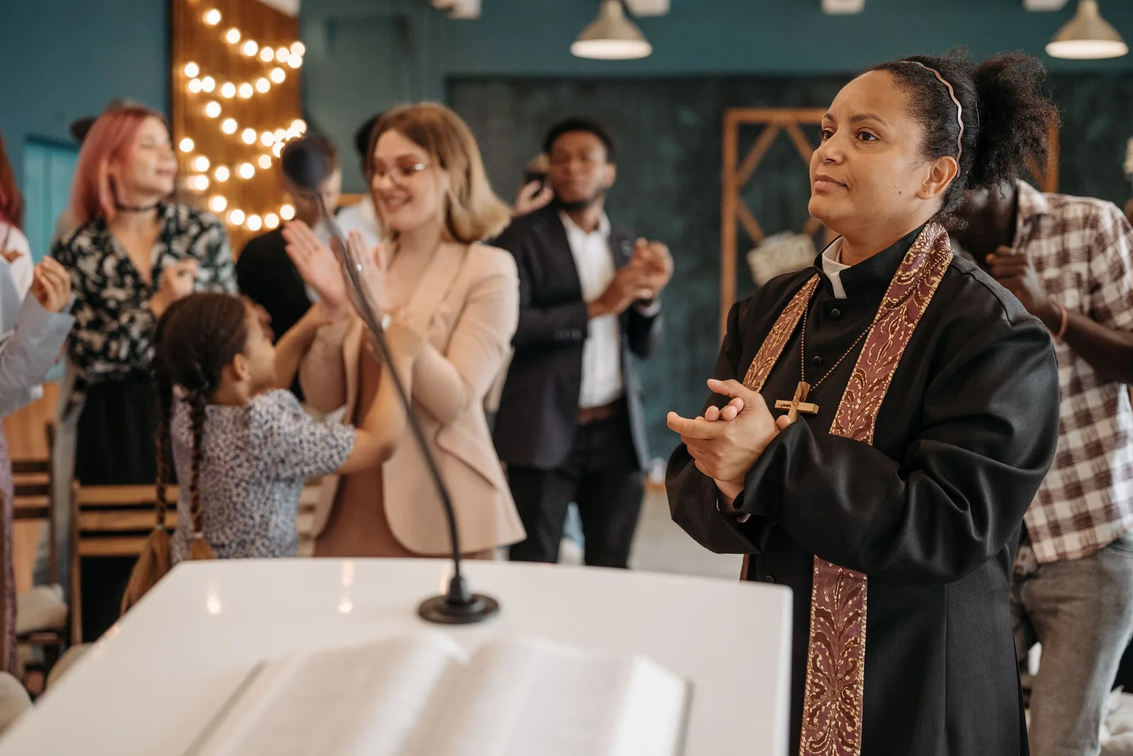 A diverse congregation clapping during a church ceremony led by a female pastor. Photo by Pavel Danilyuk on Pexels
