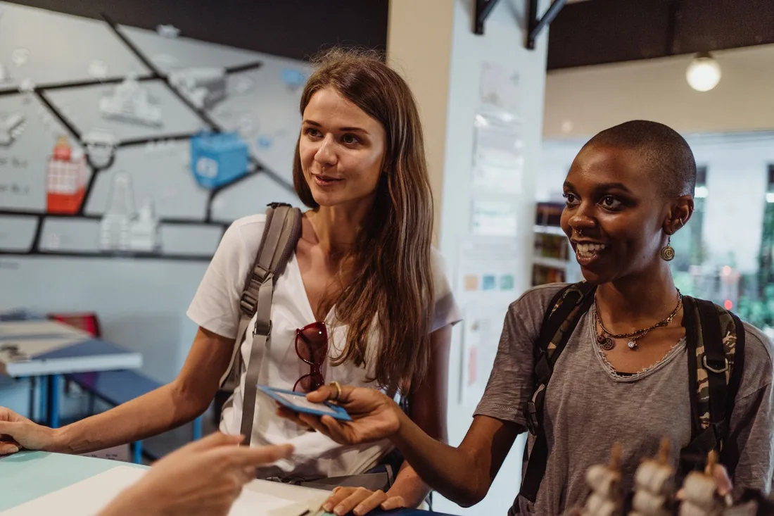 Two smiling women travelers checking in at a hotel front desk. Photo by Ketut Subiyanto on Pexels