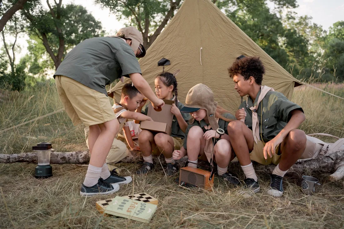A group of young scouts gathers around a tent, exploring and bonding during a summer camping trip. Photo by cottonbro studio on Pexels