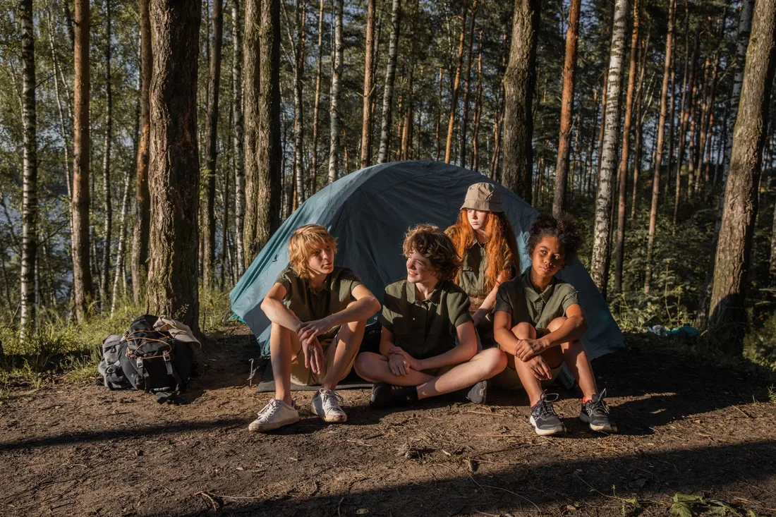 Four children sitting by a tent in the forest enjoy a camping adventure. Photo by KATRIN  BOLOVTSOVA on Pexels