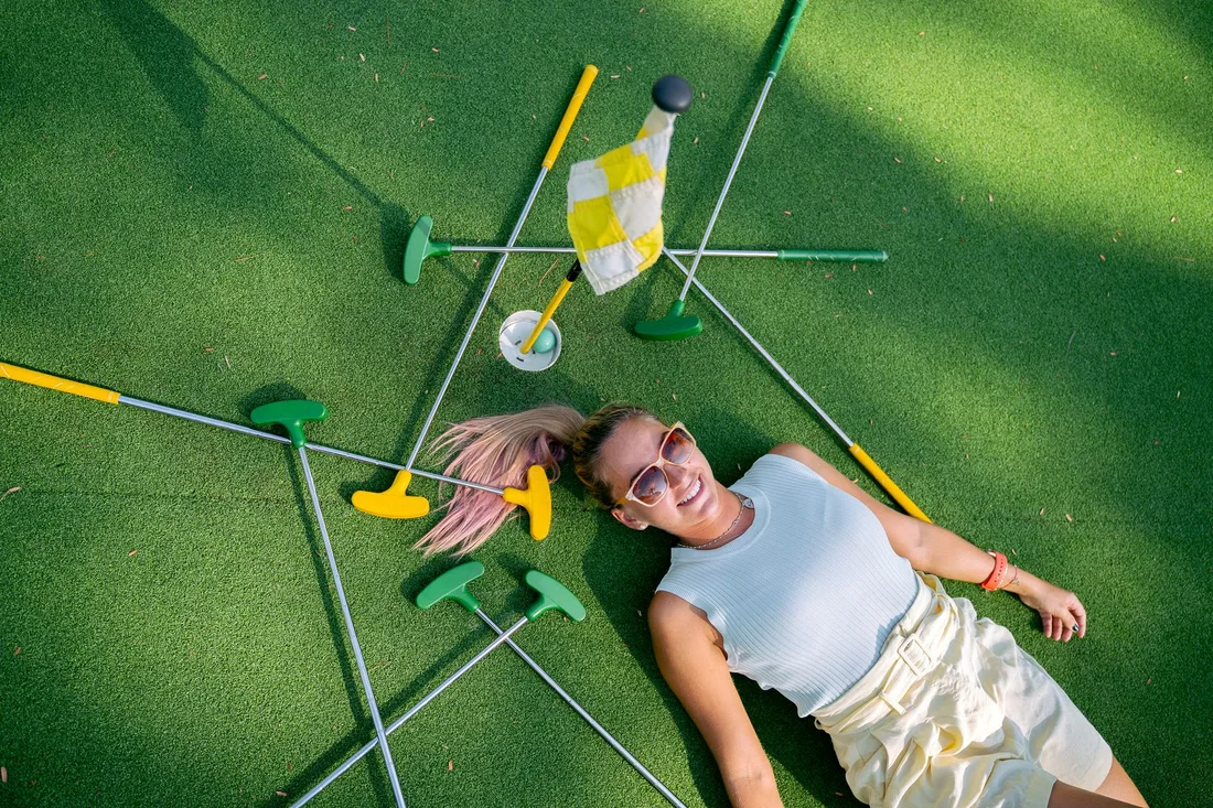 Woman enjoying a sunny day at the mini golf course, surrounded by putters and a flag. Photo by Anna Tarazevich on Pexels