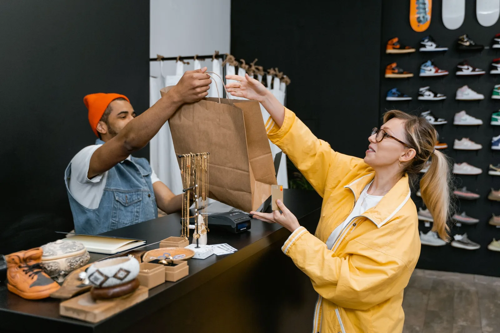 A customer and cashier exchange items at a fashionable sneaker store counter. Photo by MART  PRODUCTION on Pexels