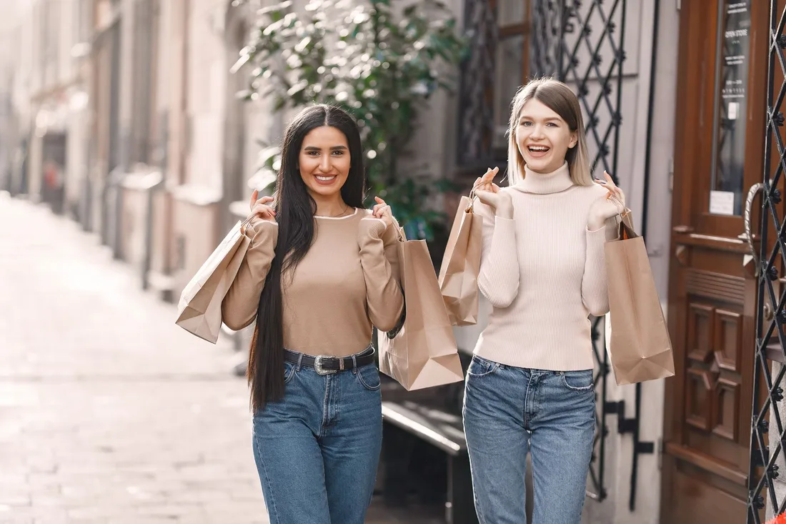 Two smiling friends holding shopping bags on a city street. Photo by Gustavo Fring on Pexels