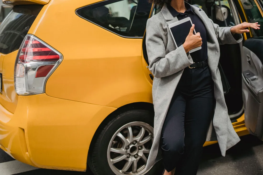 Woman in a gray coat stepping into a yellow taxi on a city street. Photo by Roberto Hund on Pexels