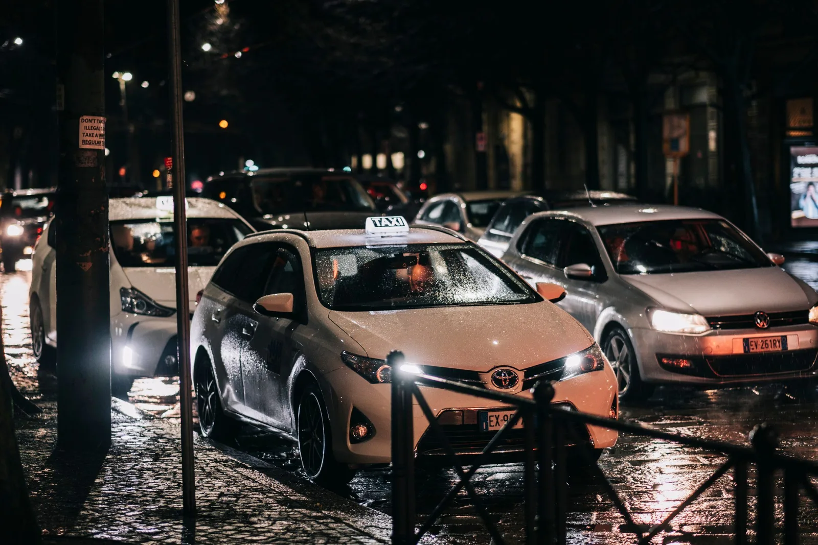 Busy city street at night with cars and taxis on a wet road, reflecting lights. Photo by Lory.captures / Lorenzo Messina on Pexels
