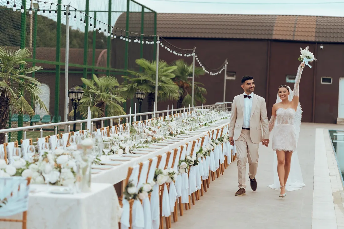 Wedding couple walking between long decorated reception tables at an outdoor venue. Photo by Eko Agalarov on Pexels