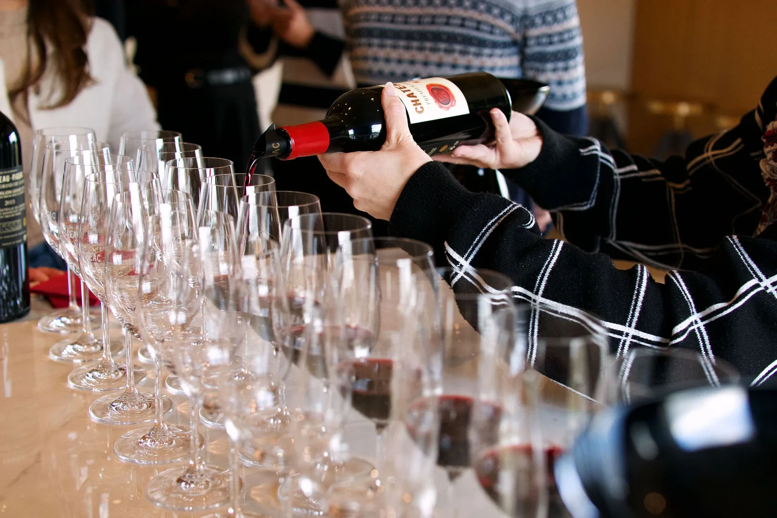 Sommelier pouring red wine into a long row of tasting glasses. Photo by Liv Kao on Pexels