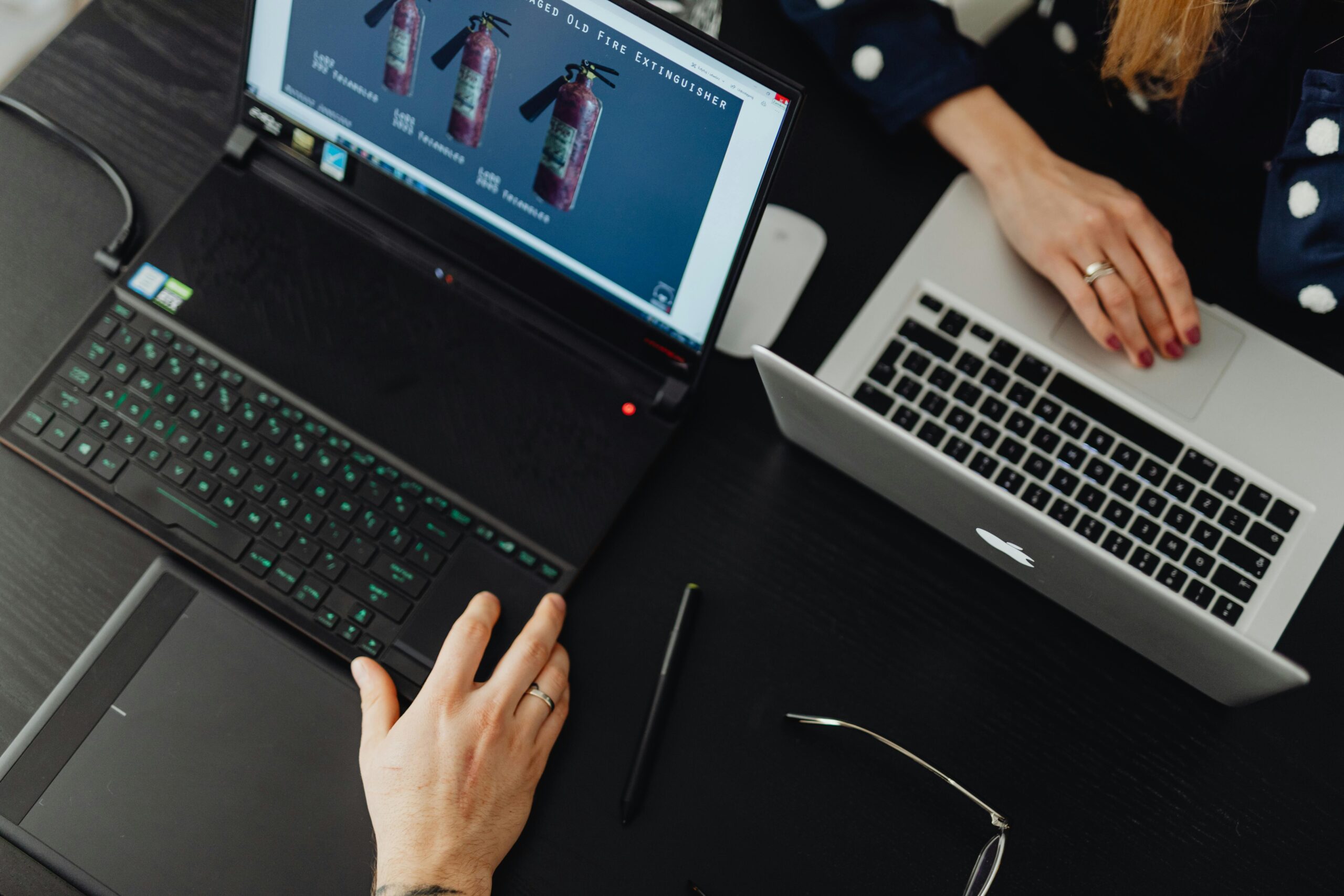 A high-angle view of two people working on laptops at an office desk, showcasing teamwork and technology. A high-angle view of two people working on laptops at an office desk, showcasing teamwork and technology.